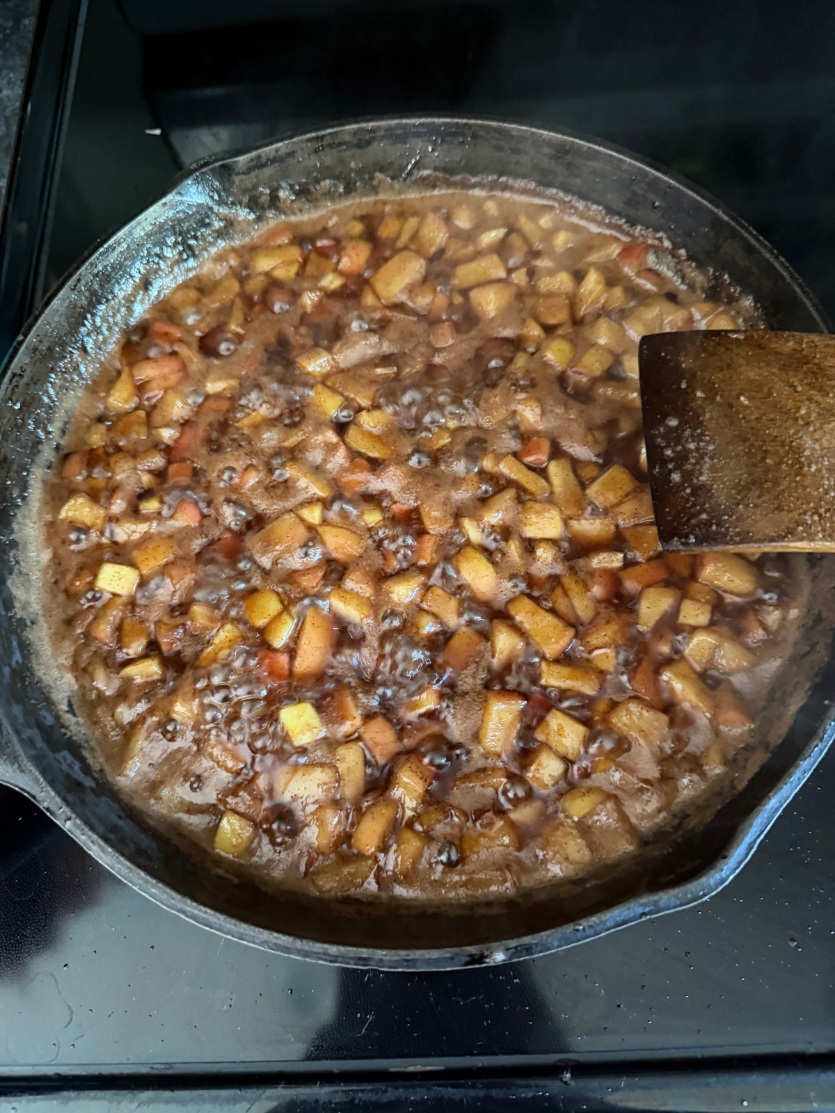 Apple pie filling is shown cooking in a cast iron skillet. 