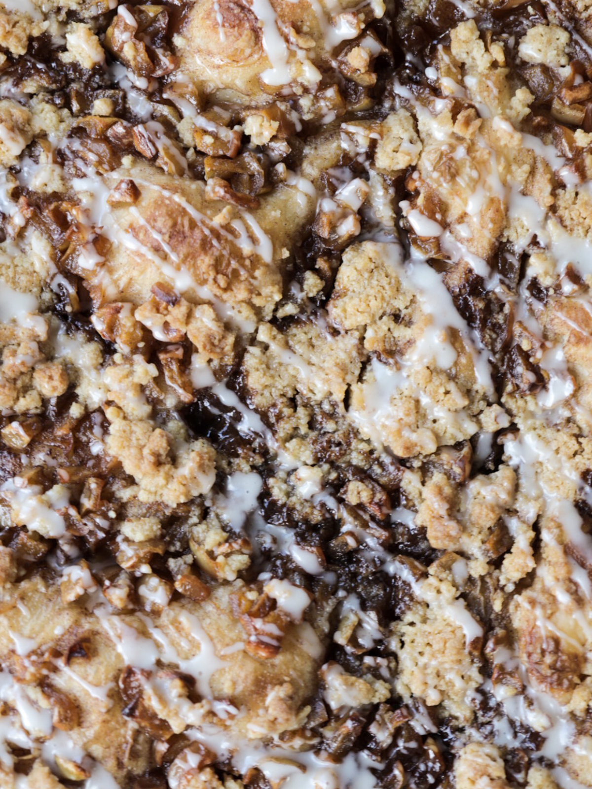 A closeup of the sourdough apple crumble focaccia is shown with vanilla icing drizzled over it.