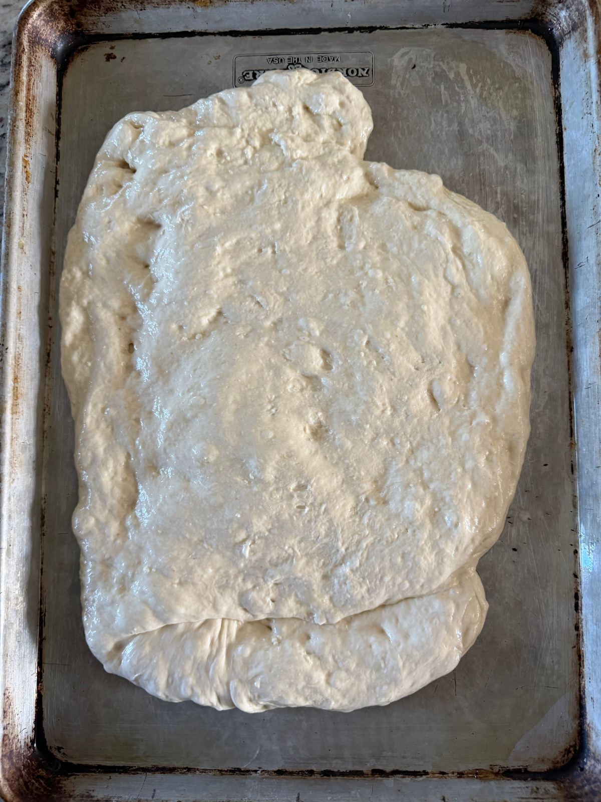 Sourdough apple streusel focaccia sits on a greased baking sheet with half the apple pie filling folded inside.