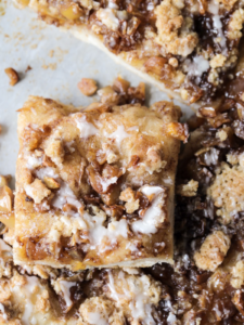 A closeup of a slice of sourdough apple streusel focaccia is shown with a vanilla icing drizzled over it.