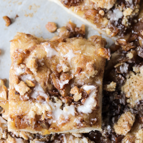 A closeup of a slice of sourdough apple streusel focaccia is shown with a vanilla icing drizzled over it.
