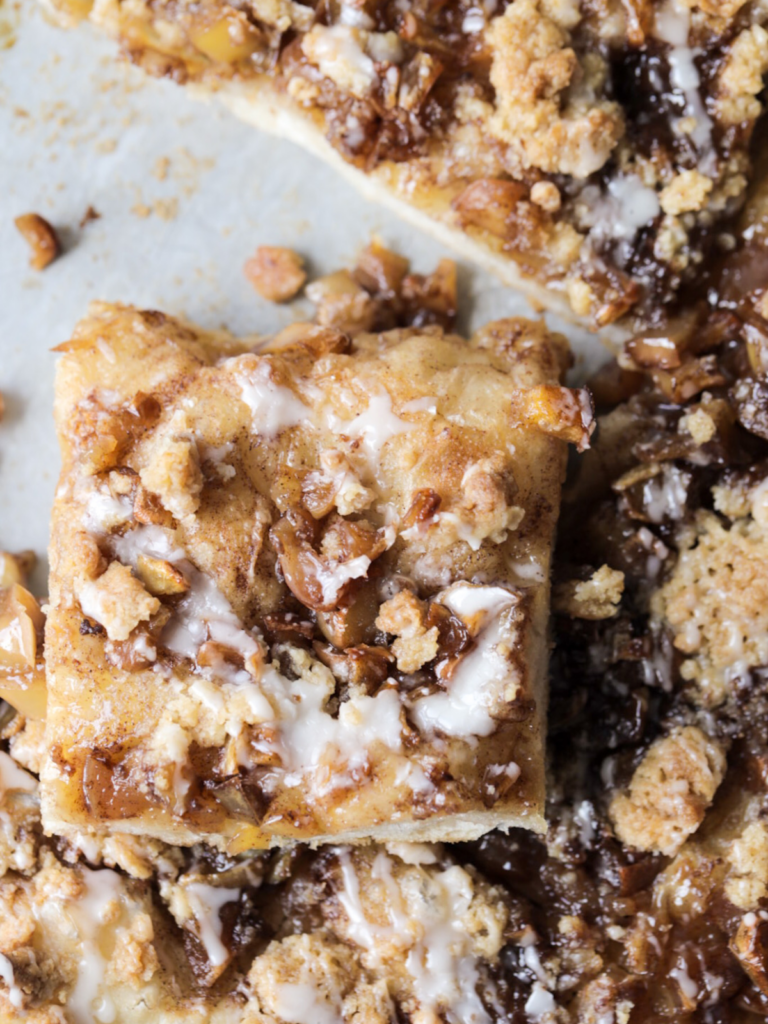 A closeup of a slice of sourdough apple streusel focaccia is shown with a vanilla icing drizzled over it.