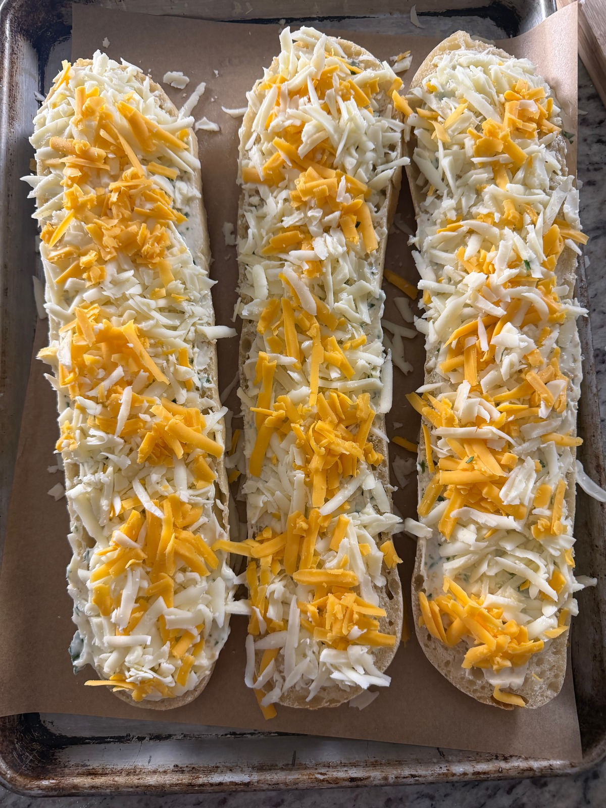 Sourdough french bread is shown with the freshly grated cheese over it before it goes in the oven.