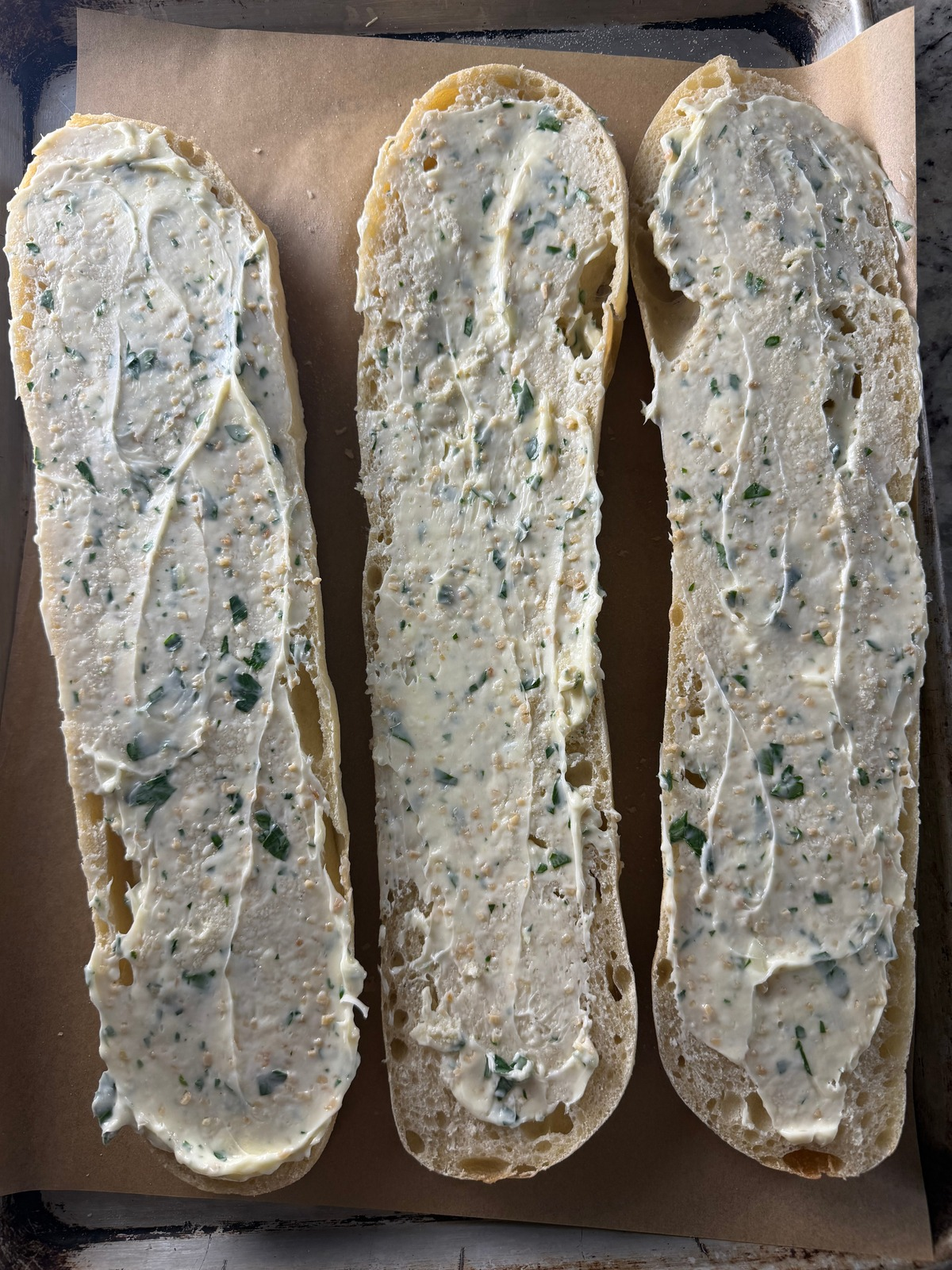 The sourdough french bread is shown sliced in half with garlic herb butter spread over it.