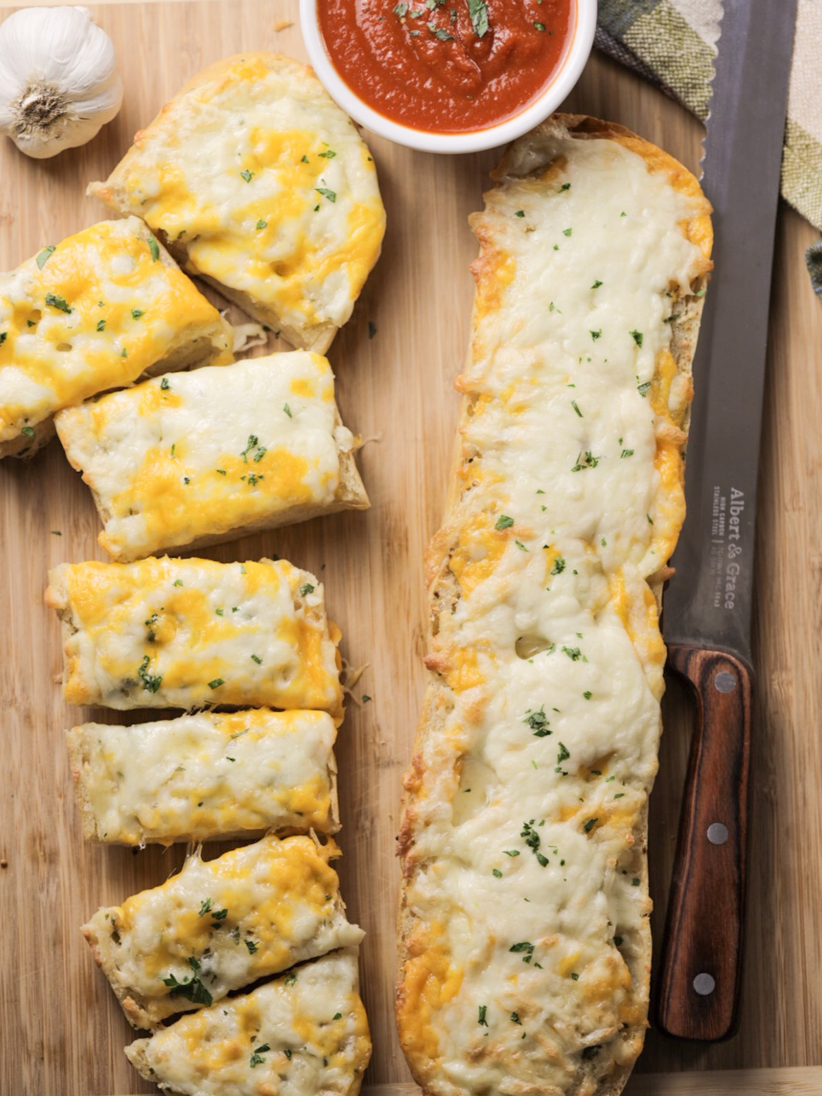 The freshly baked sourdough cheesy garlic bread is shown on a wooden cutting board. One slice is sliced into separate servings and the other is whole.