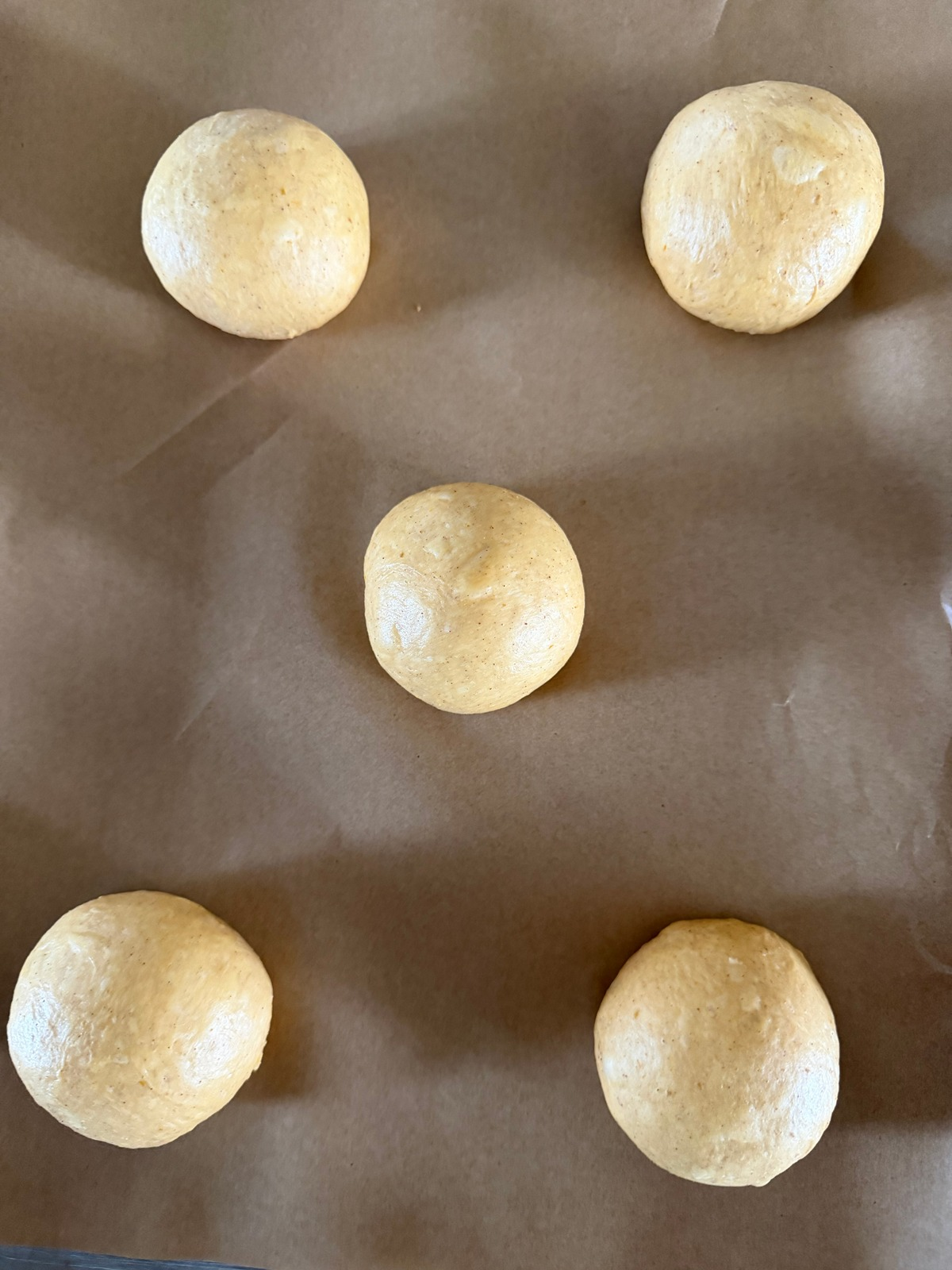 The sourdough pumpkin kolache dough has been shaped into balls. They rest on a parchment lined baking sheet.