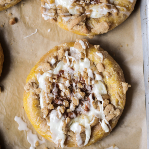 A closeup of a sourdough pumpkin cream cheese kolache is shown with vanilla icing drizzled over it.