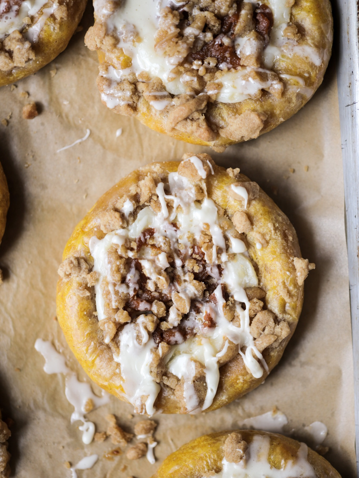 A closeup of a sourdough pumpkin cream cheese kolache is shown with vanilla icing drizzled over it.